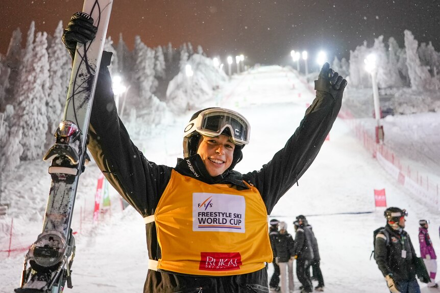Jakara Anthony holds up her skis in front of a flood-lit ski slope