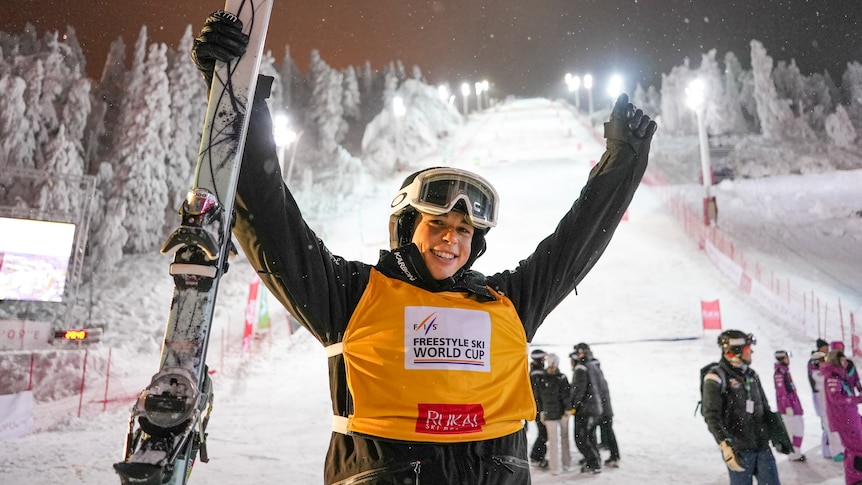 Jakara Anthony holds up her skis in front of a flood-lit ski slope