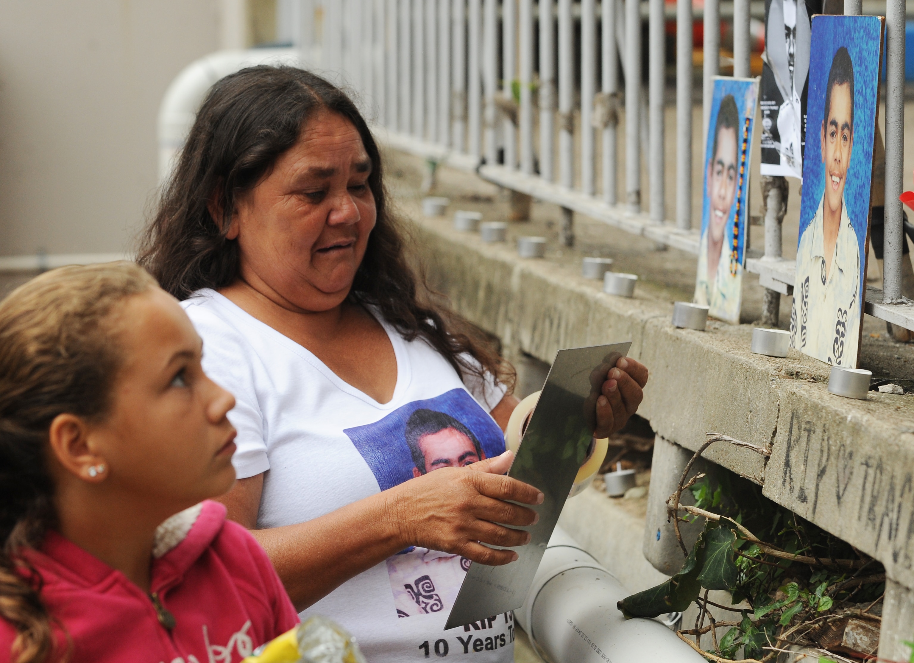 a woman with brown curly hair and shirt with a photo of her son places photo on brick ledge