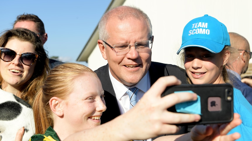 Scott Morrison poses for a selfie with two young girls, one wearing a Team ScoMo hat