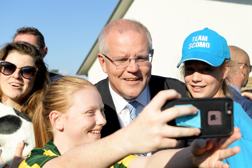 Scott Morrison poses for a selfie with two young girls, one wearing a Team ScoMo hat