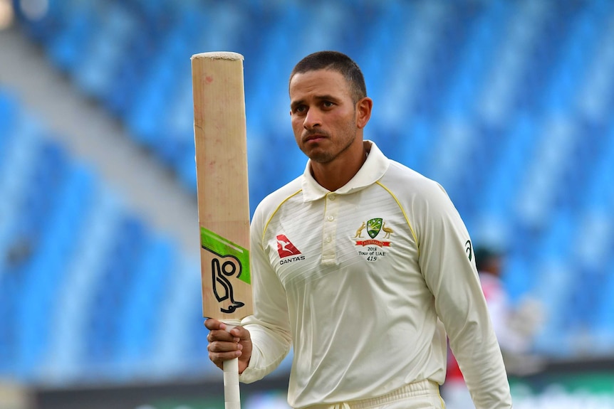 Tight telephoto shot of a cricket batsman raising his bat as he leaves the field.