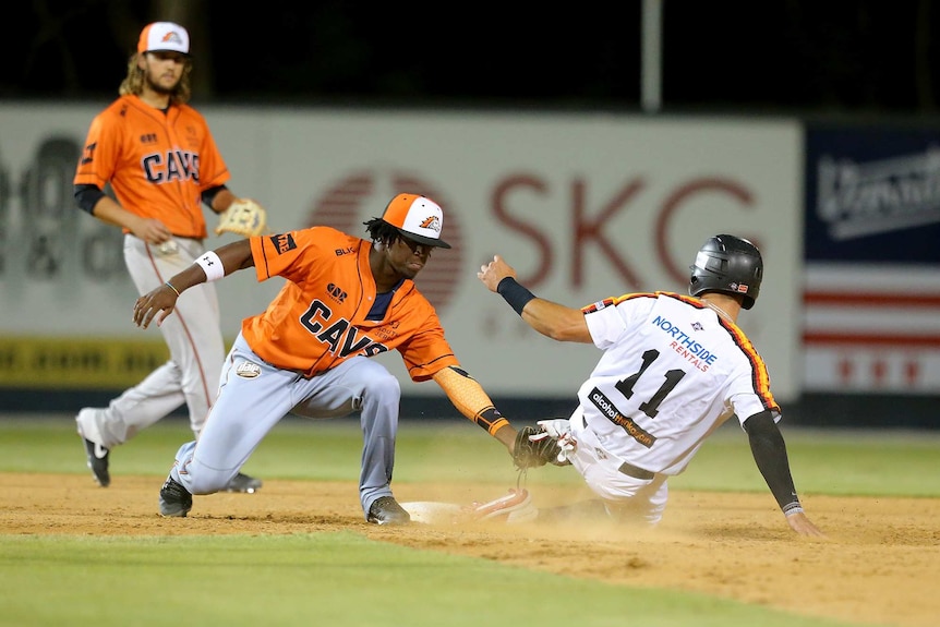 A Perth Heat baseballer slides into base as a Canberra Cavalry player tries to tag him.