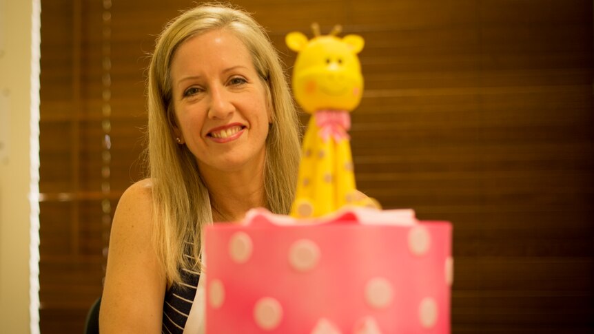 A woman sits behind an ornately decorated children's birthday cake.
