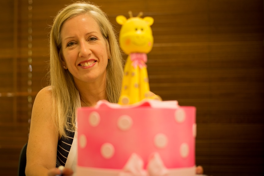 A woman sits behind an ornately decorated children's birthday cake.