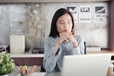 Young woman at her desk in front of a laptop looking unhappy.