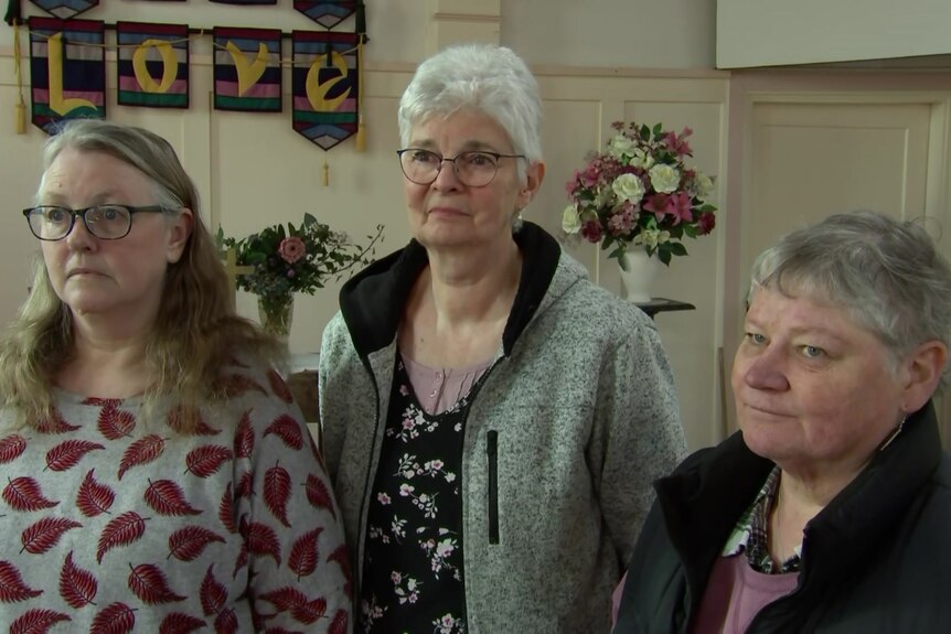 Three women standing in a church with flowers in the background.