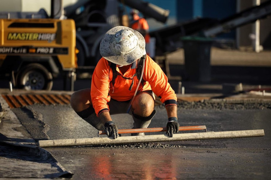 Рабочий выравнивает бетон при заливке плит на строительной площадке на Радар-стрит в Литтоне в Брисбене.