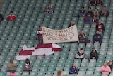 Manly fans hold a sign reading 'GUESS WHAT? MANLY HATES YOU TOO!!!' in the stands before a game.