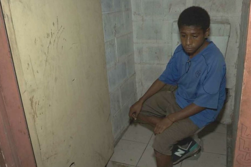 A boy is seen sitting in a toilet cubicle.