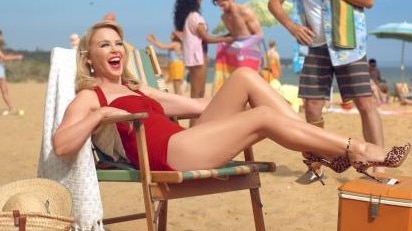 Kylie Minogue lies on a chair with a towel in a red swimsuit on Sandringham Beach.