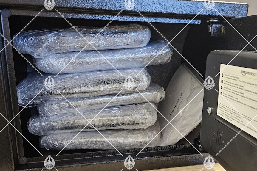 A photo of cocaine bags in a black safe with a piece of paper.