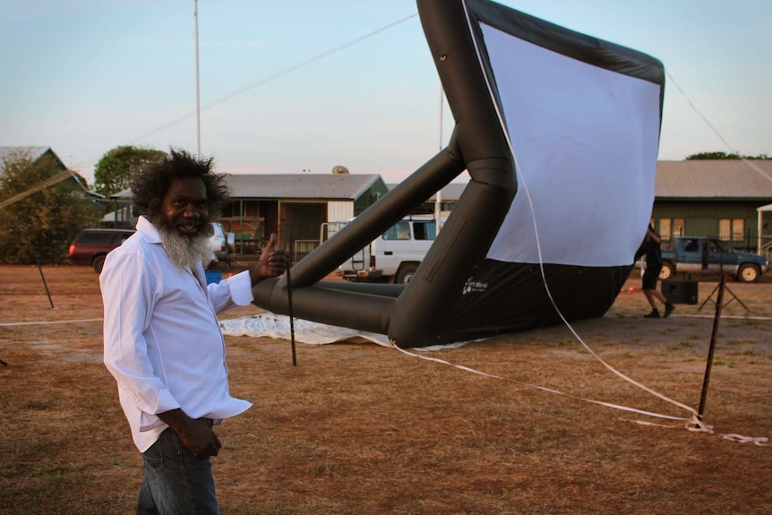 Witiyana Marika in Gunbalanya gives the thumbs up at the local footy oval with a blow up projector behind him