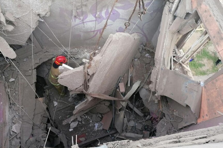 Rescue worker carefully shifts through collapsed ceiling on the floor of a residential apartment unit hit by air strikes.