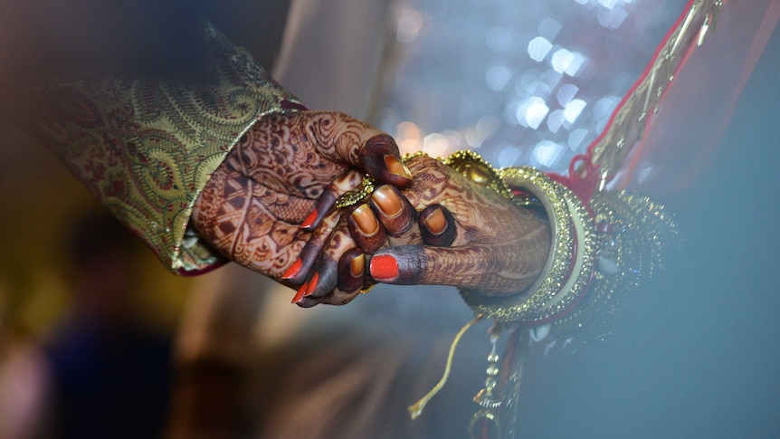 a close up of a man's hand holding a woman's hand, dressed in traditional Indian wedding wear and decorated in henna