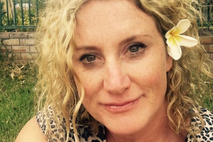 A woman in a leopard print top with a flower in her hair takes a selfie in a garden.