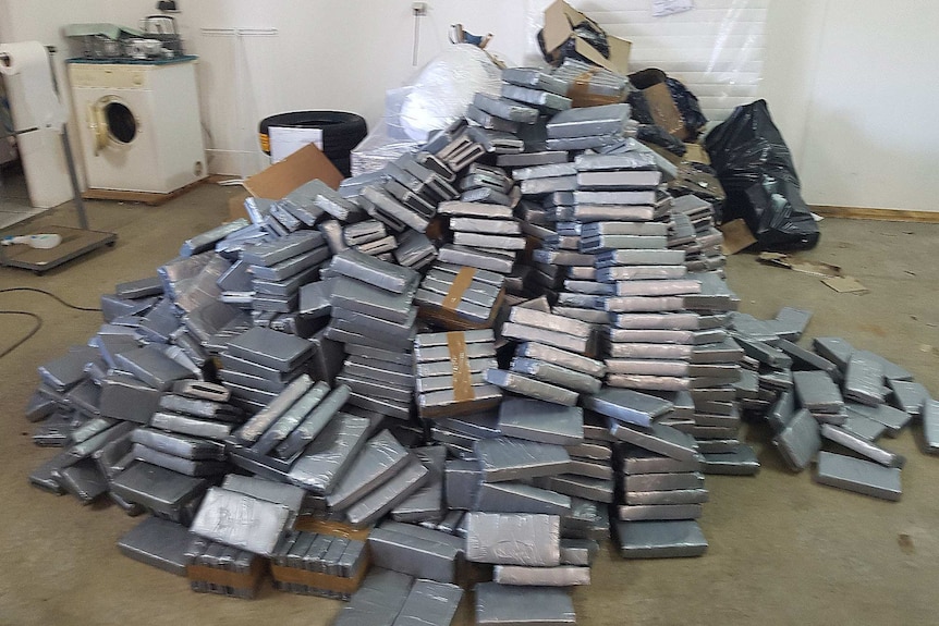 A large pile of rectangular packages wrapped in silver plastic is shown on the floor of a room.