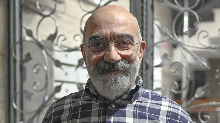 middle aged man with short beard and spectacles, in a checked shirt, smiling at the camera