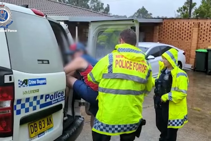Man climbing into police vehicle after being arrested by two police wearing high vis shirts