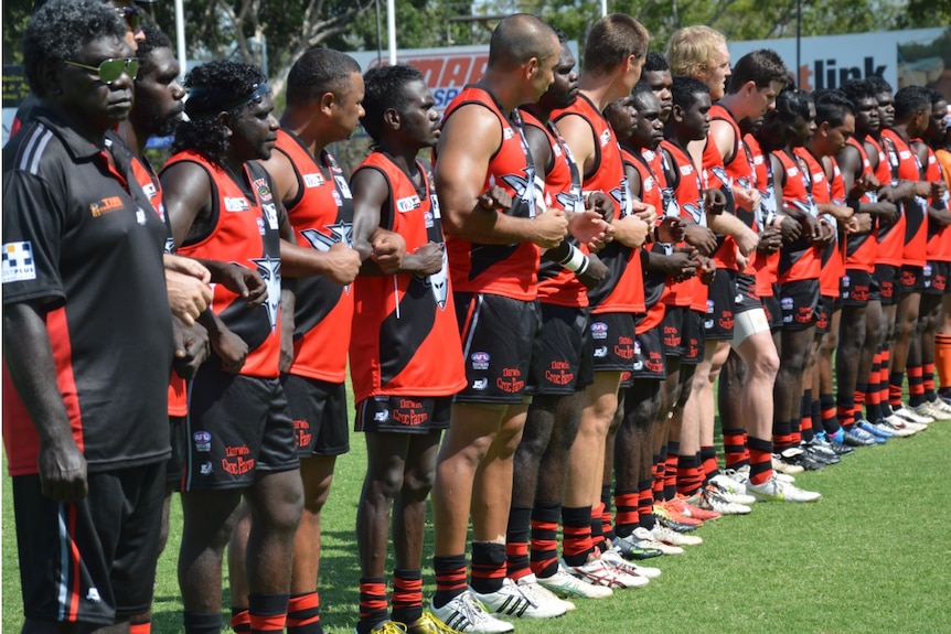 Tiwi Bombers footy players line up with linked arms
