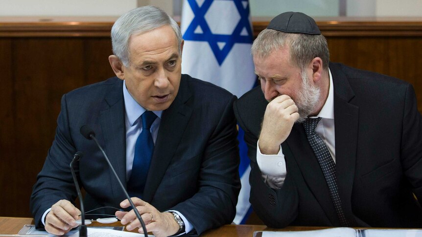 Benjamin Netanyahu speaks with Avichai Mandelblit, who is wearing a black kippah, with an Israeli flag in the background