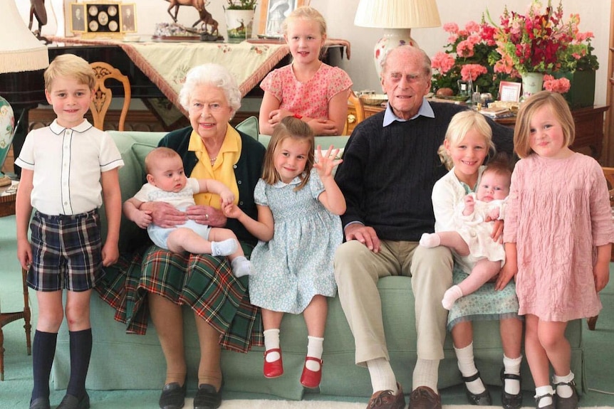 Queen Elizabeth II and Prince Philip sit on a sofa surrounded by young children.
