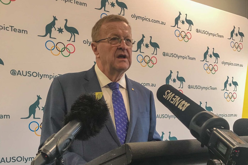 John Coates stands in front of a lectern and speaks.