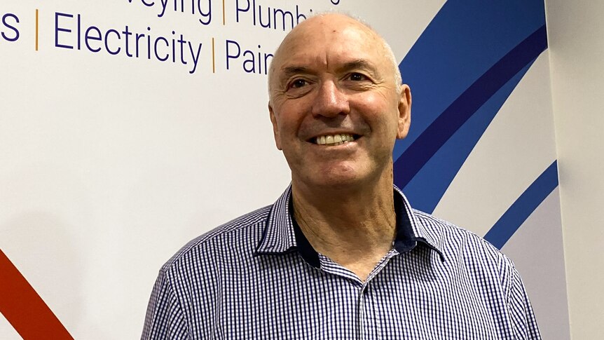 Man in blue striped shirt in front of agency sign, smiling