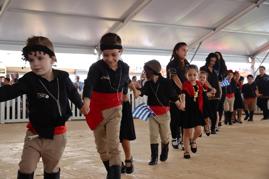 A line of young kids in Greek costume dance together.