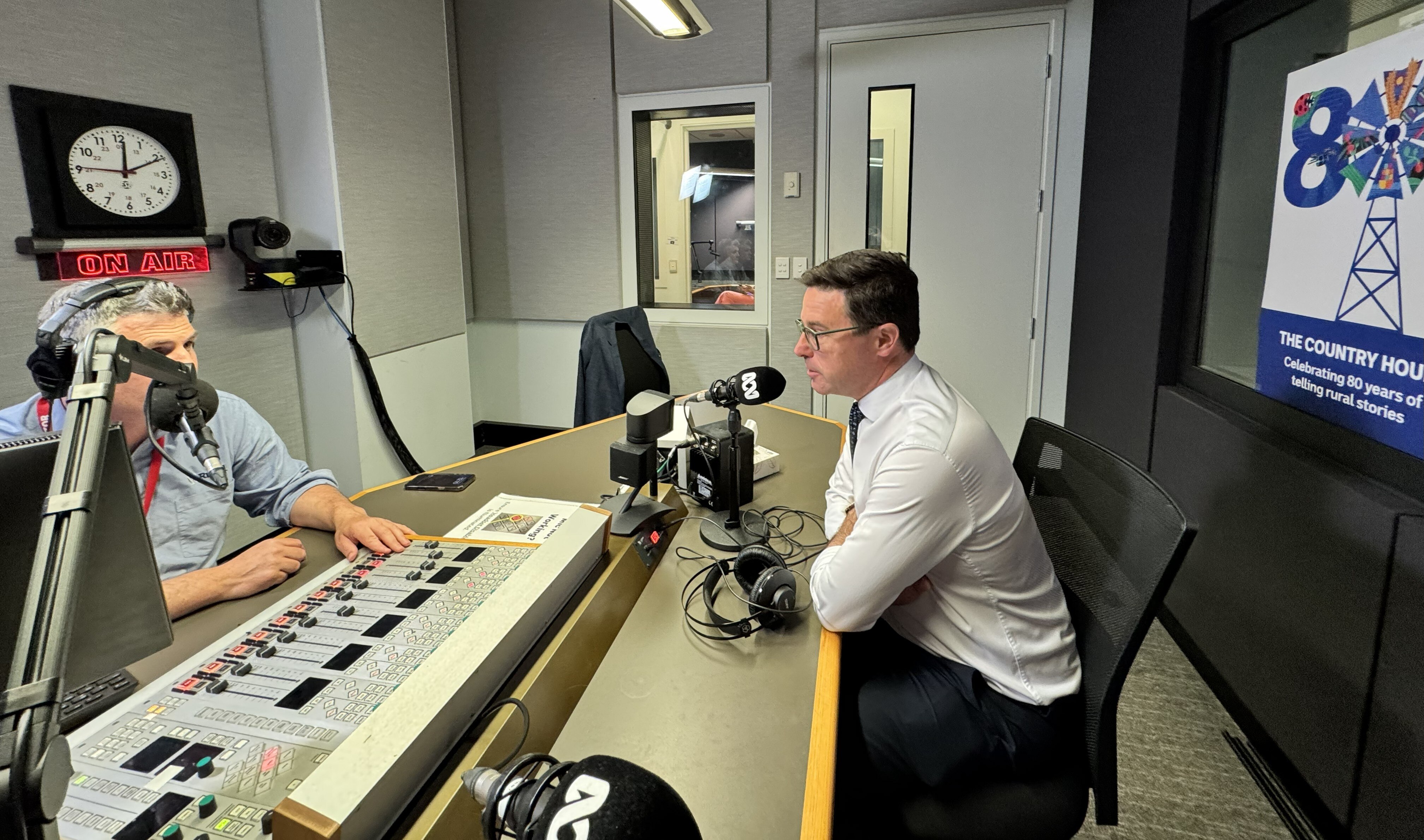 Mid shot of a radio studio, two mean on either side of the desk in front of microphones