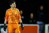 A boy stands in an orange goalkeeper's football kit during an Australia Cup match for Oakleigh Cannons.