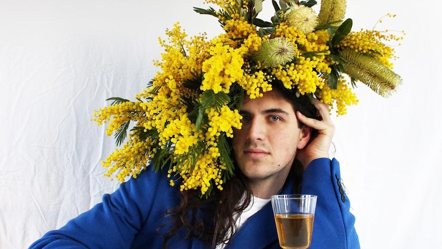 Jake Kuit sits with a wattle headpiece, wearing a blue blazer and with his hand on a white wine.