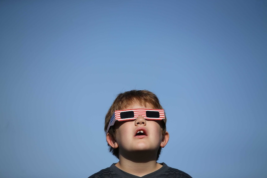 A boy uses solar viewing glasses as the sun emerges through fog cover before the solar eclipse in Depoe Bay, Oregon.