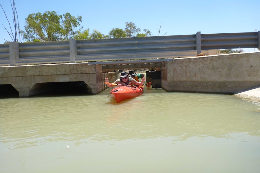 A man passes under a concrete water regulator lying on his stomach on his orange canoe