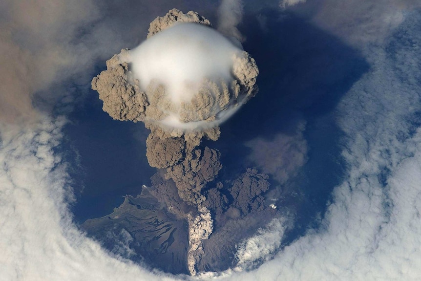 Dramatic photo from above of the Sarychev Volcano erupting, large grey clouds of ash rising above