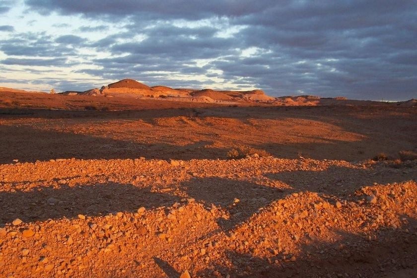 A picture of piles of red dirt in front of hills at sunrise.