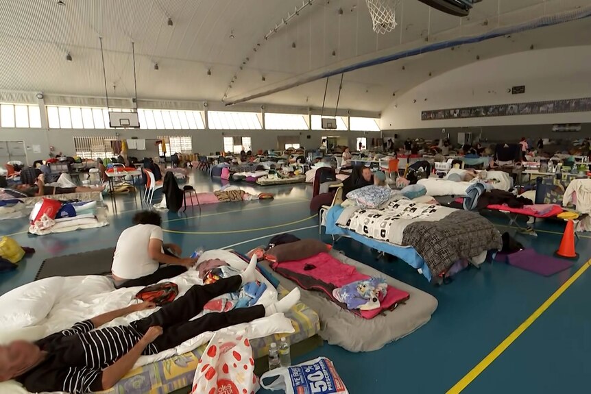 An indoor basketball court filled with people, beds and belongings.