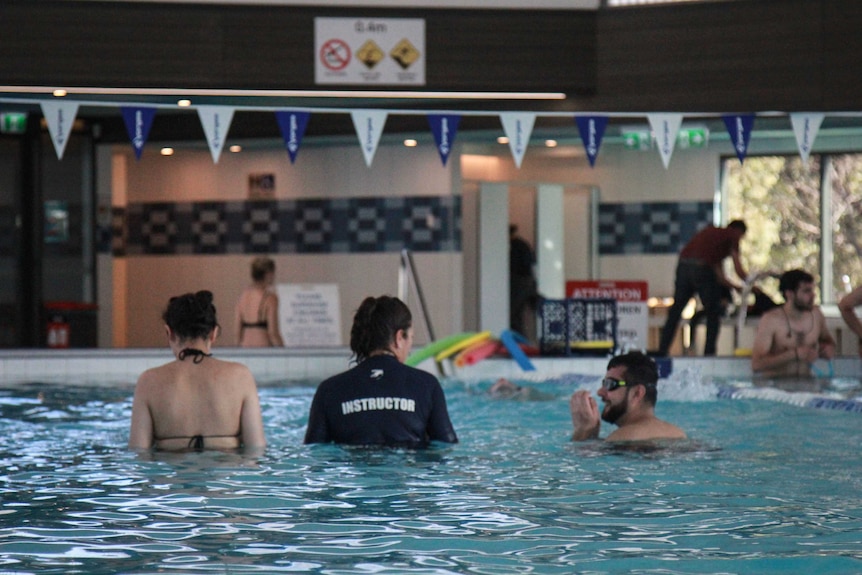 Three people, one in an instructor shirt, wade chest-deep in a pool inside the Leichhardt Aquatic Centre.