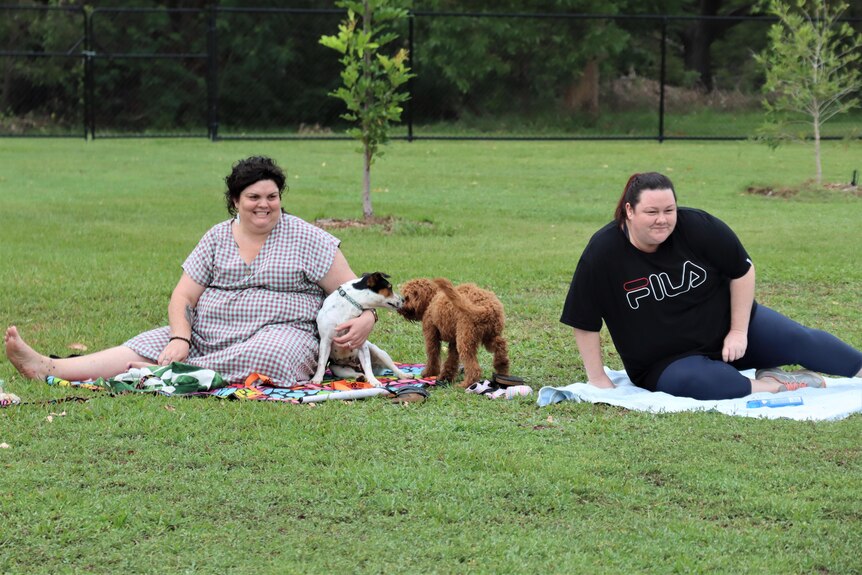 Two women sitting in a dog park with dogs.
