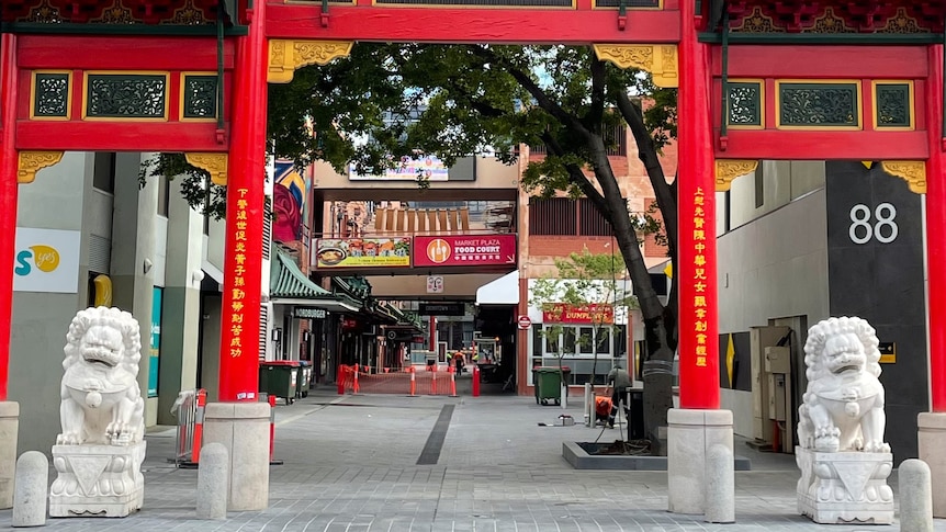 A large red gate-like entrance to a street with concrete lions either side