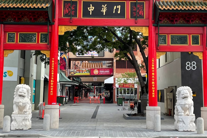 Une grande entrée en forme de porte rouge dans une rue avec des lions en béton de chaque côté