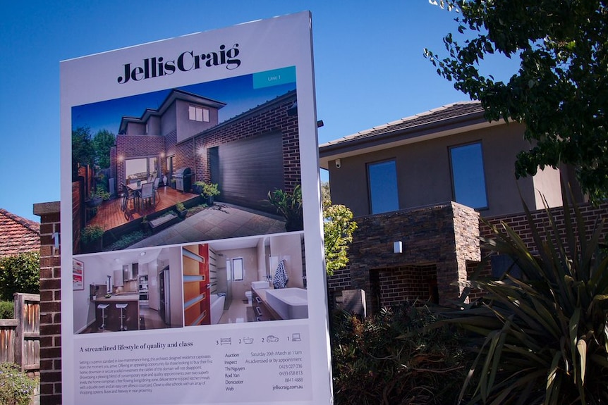 A large white for sale' sign with images of a house in front of a brick home.