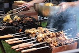 Barbecued meats including on skewers being cooked.