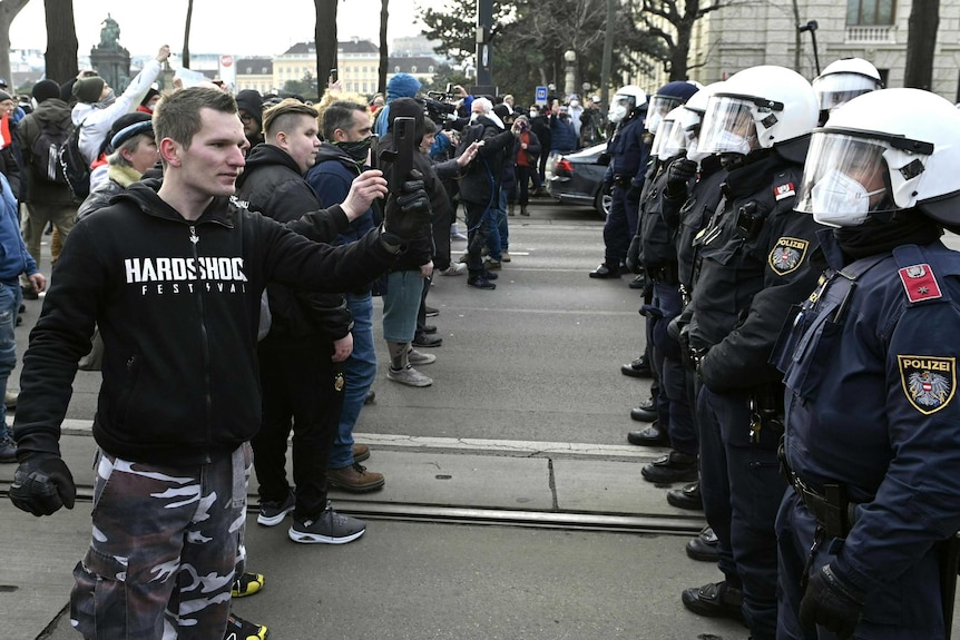 Protesters, some without masks, take pictures of a line of police during a demonstration against COVID restrictions in Vienna.