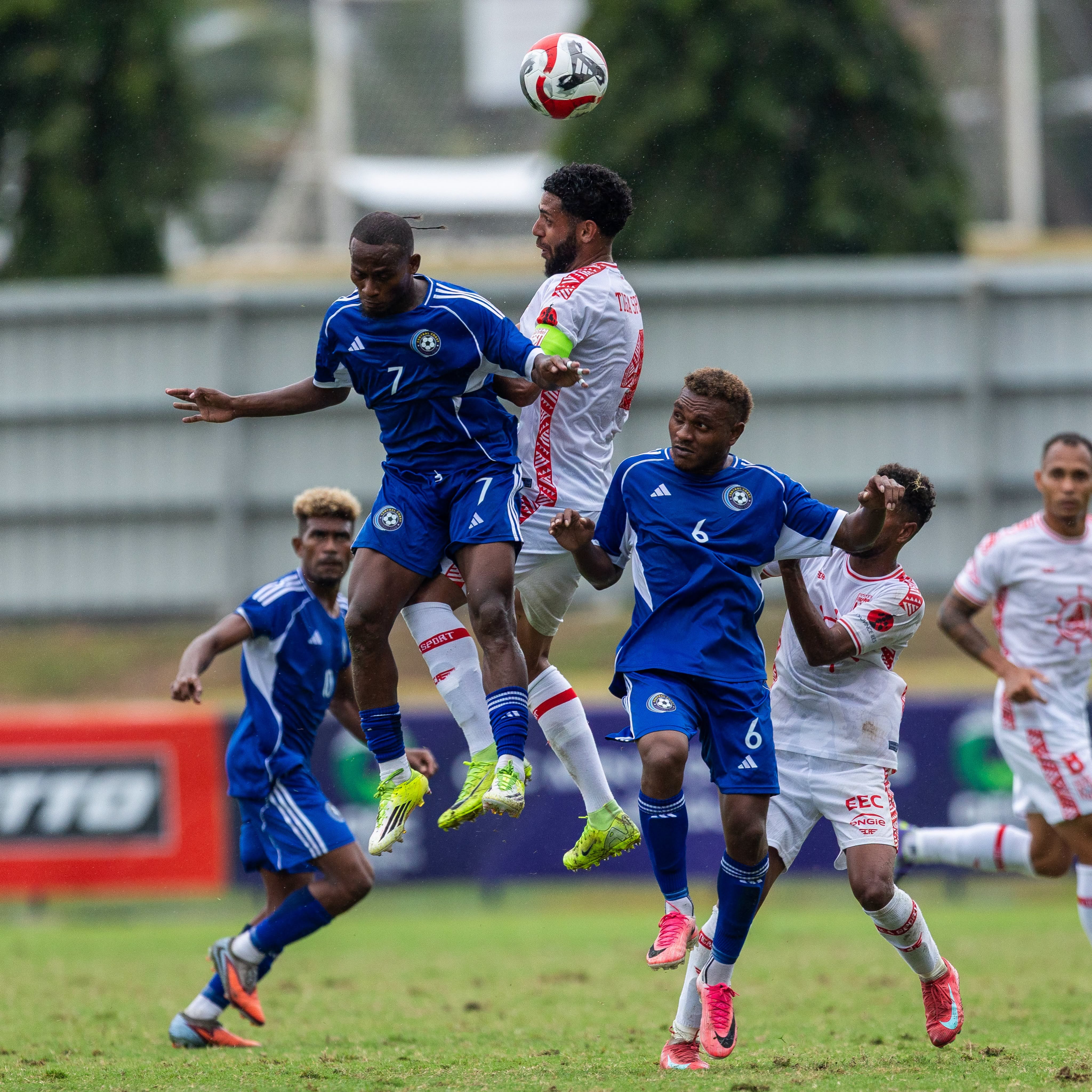 Solomon Island and New Caledonia soccer players jump up in the air as they go for the ball on a soccer field in Ba, Fiji