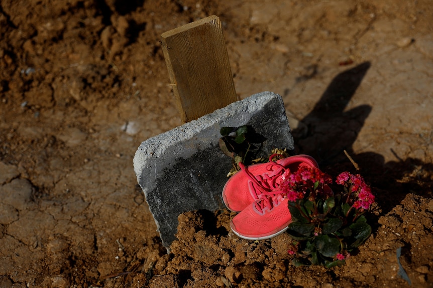 A pair of bright pink shoes and flowers on top of a grave.
