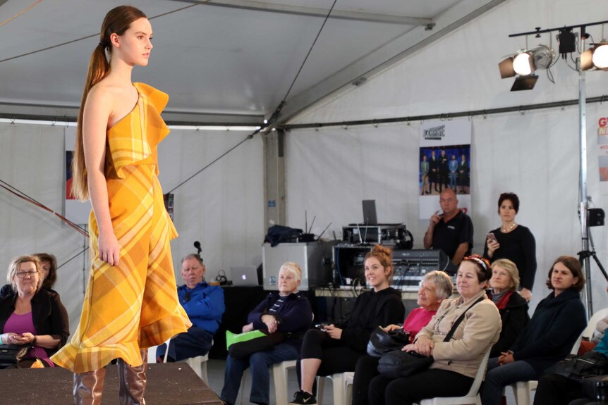 A model on the catwalk in a yellow merino dress.