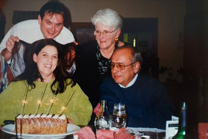 An old photo of two adults and two older people laughing sitting around a table with a birthday cake on it.