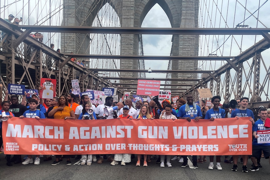 Protesters cross Brooklyn Bridge holding a banner saying 'March Against Violence'.