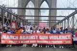 Protesters cross Brooklyn Bridge holding a banner saying 'March Against Violence'.